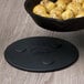 A black Lodge magnetic trivet holding a black pan with food on a wood surface.