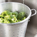A Town aluminum colander filled with broccoli being rinsed under running water.