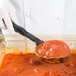 A person in white gloves using a Vollrath black nylon oval spoon to serve red sauce.