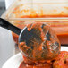 A black Vollrath High Heat Spoodle spoon filled with meatballs in red sauce.