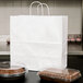 A Duro white paper shopping bag with handles holding a tray of food with a brown cake and a clear plastic cover.