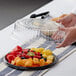A person holding a Visions clear plastic lid over a plate of fruit.