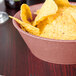 A paprika polyethylene round basket filled with potato chips on a table in a Mexican restaurant.