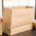 A Duro natural kraft paper bag with handles on a counter next to food.