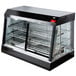 A black and silver Vollrath countertop hot food display case with glass doors on a counter with two racks inside.