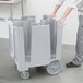 A person pushing a large grey plastic Cambro dish caddy.