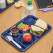 A dark blue Carlisle compartment tray with a sandwich, carrots, apples, and a drink.