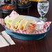 A blue oval deli server filled with tacos and salsa on a table with a red and white checkered tablecloth.