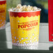 A yellow Carnival King popcorn bucket on a table filled with popcorn with a red and white label.