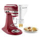 A white KitchenAid stand mixer with a KitchenAid pasta attachment and a bowl of pasta on it.