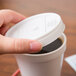 A person holding a Dart white plastic sip thru lid over a cup of coffee.