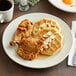 An Acopa ivory stoneware plate with waffles and fried chicken on a table.