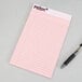 A pink TOPS Prism+ narrow ruled notepad with lines and a pen.