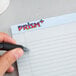 A hand holding a pen over a TOPS Prism narrow ruled notepad.