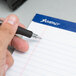 A person holding a black pen over an Ampad wide ruled writing pad on a table.