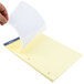 A hand holding a medium ruled yellow sheet of paper with a pen.