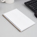 A white wirebound TOPS notebook with green accents on a desk with lined paper.