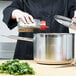 A chef pouring seasoning into a Vollrath stainless steel sauce pan on a counter in a professional kitchen.