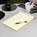 A yellow Ampad Law Ruled writing pad on a table with a pen and cup of pens.