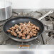 A Vollrath Optio stainless steel non-stick fry pan with meat and onions cooking on a stove.