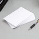 A stack of white unruled index cards next to a pen.