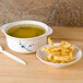 A Thunder Group Blue Bamboo melamine miso bowl with broth and a plate of food on a wooden table.