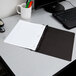A desk with a black Oxford clear front report cover with a notebook and pen inside