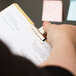 A person's hand holding a clipboard with sticky notes secured by a X-Acto Bulldog clip.