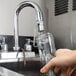 A hand using a Regency Hands-Free Faucet Wand to fill a glass jar on a counter.