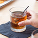 A person's hand holding a Libbey rim tempered rocks glass filled with brown liquid and a straw.