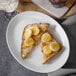 A white oval melamine platter with toast, bananas, and honey on it.