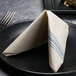 A folded white napkin with a blue dish towel print on a black plate next to a fork.