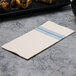 A Hoffmaster white and blue dishtowel print dinner napkin on a table with food and a knife.