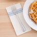 A white Hoffmaster dinner napkin with a blue dishtowel print and a fork on a plate with a waffle.