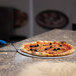 A pizza with black olives being cut on a GI Metal pizza tray.