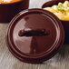 A Bon Chef burnt umber porcelain lid with a handle on a brown surface.