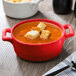 A red Bon Chef porcelain oval cocotte filled with soup and croutons.