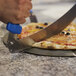 A person using a GI Metal stainless steel pizza rocker knife to cut a pizza.