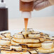 A person using a Tablecraft squeeze bottle to pour syrup on a plate of pancakes.