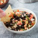 A person holding a chip dipping it into a bowl of black bean and corn salsa.