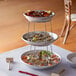 A three tiered seafood tower with mini aluminum trays on a stand full of seafood.