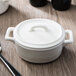 The white porcelain lid for a Bon Chef oval cocotte with a handle and spoon inside.