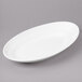 A white Bon Chef oval porcelain plate with a rim on a gray surface.