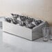 A stainless steel flatware organizer with spoons in it.