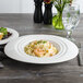 A white Bon Chef porcelain oval pasta bowl filled with pasta and salad on a table.