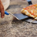 A person using a GI Metal triangular pizza server to cut a pizza.