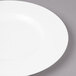 A close-up of a Bon Chef white bone china bread and butter plate with a wide white rim on a gray surface.