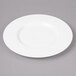 A white Bon Chef bone china bread and butter plate with a wide rim on a gray surface.