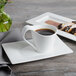 A white Bon Chef bone china coffee cup and saucer on a table with a cup of coffee and pastries.
