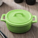 A green Bon Chef porcelain oval cocotte with a lid on a table.